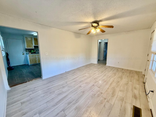 spare room featuring a textured ceiling, visible vents, baseboards, ceiling fan, and wood finished floors