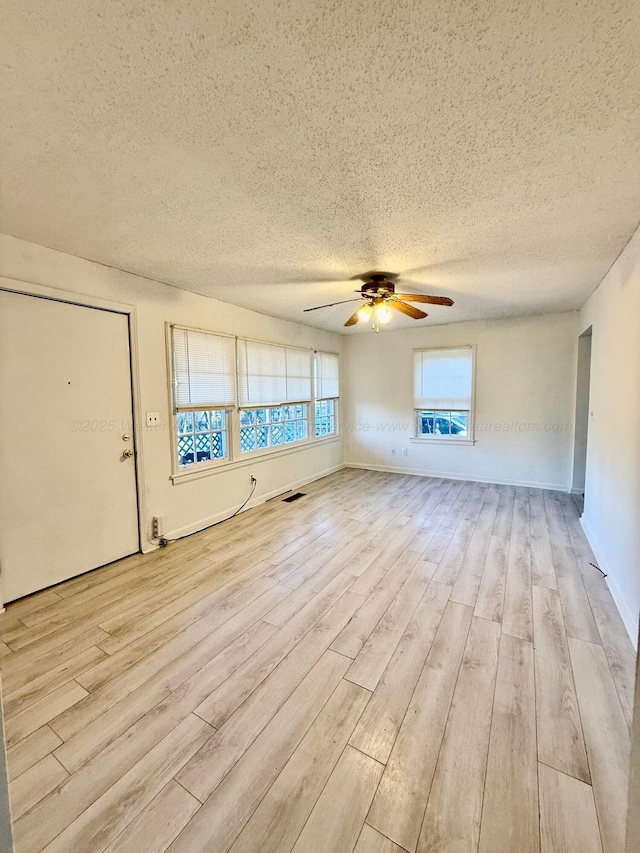 unfurnished living room with a textured ceiling, light wood-type flooring, visible vents, and a ceiling fan