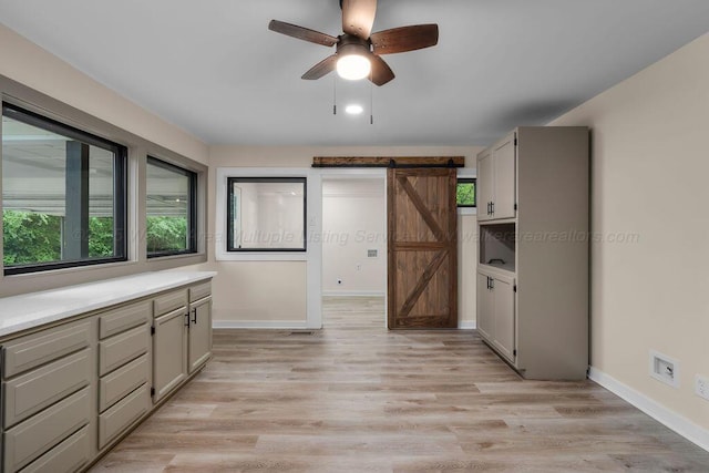 interior space with a barn door, light wood-type flooring, a ceiling fan, and baseboards