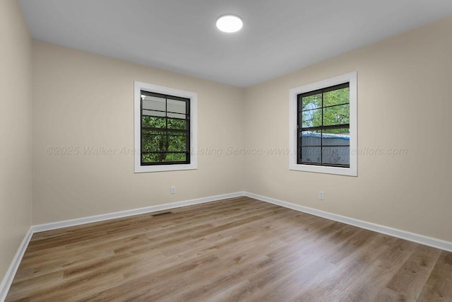 empty room with wood finished floors, visible vents, and baseboards