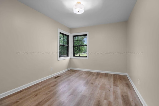 empty room featuring wood finished floors, visible vents, and baseboards