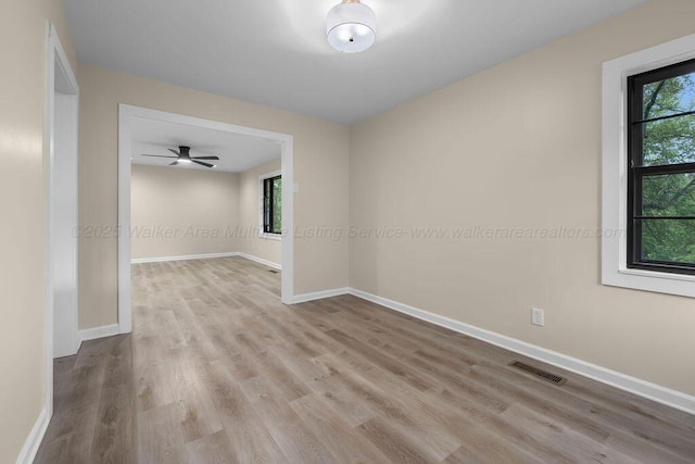 empty room featuring baseboards, a healthy amount of sunlight, wood finished floors, and visible vents