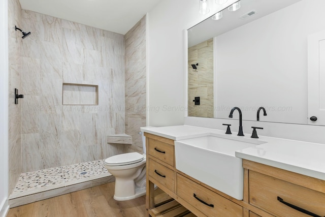 bathroom featuring toilet, visible vents, tiled shower, vanity, and wood finished floors