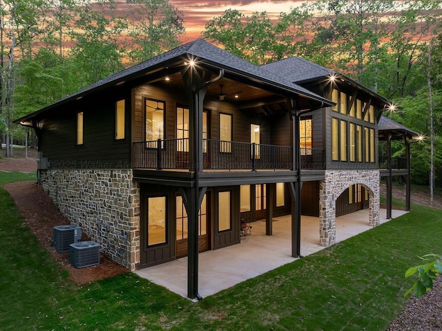 rear view of house featuring a balcony, a lawn, cooling unit, a patio, and stone siding