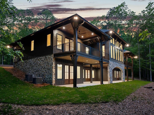 rear view of property featuring a patio area, stone siding, a balcony, a yard, and a ceiling fan