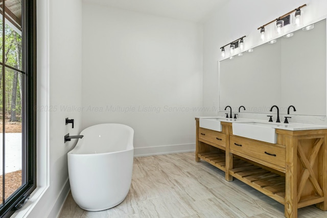 full bathroom with a sink, a freestanding bath, double vanity, and baseboards