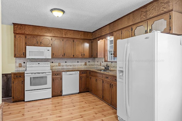 kitchen featuring a sink, a textured ceiling, brown cabinetry, light wood-style flooring, and white appliances
