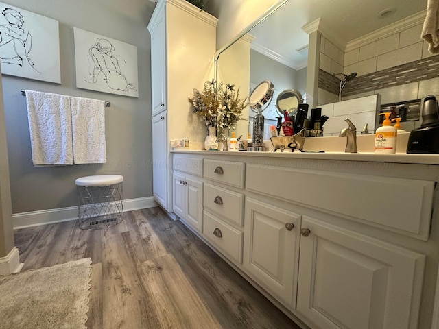 bathroom featuring crown molding, double vanity, wood finished floors, baseboards, and a tile shower