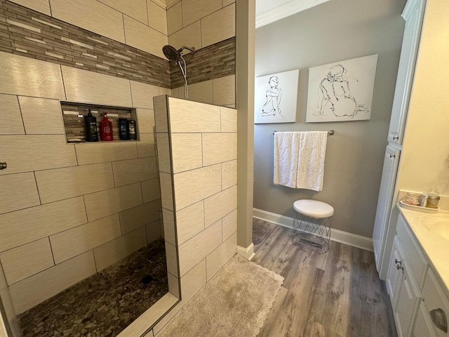 full bath featuring a walk in shower, wood finished floors, baseboards, vanity, and ornamental molding