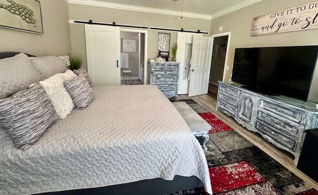 bedroom with wood finished floors, a barn door, crown molding, and ensuite bathroom