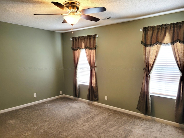 carpeted spare room with a textured ceiling, visible vents, ceiling fan, and baseboards