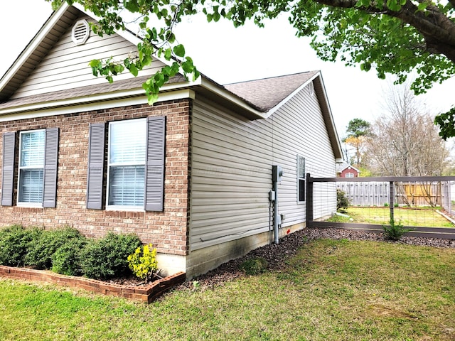 view of property exterior featuring a yard, brick siding, and fence