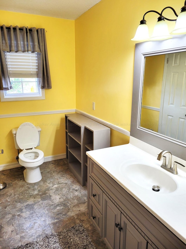bathroom featuring stone finish floor, baseboards, toilet, and vanity