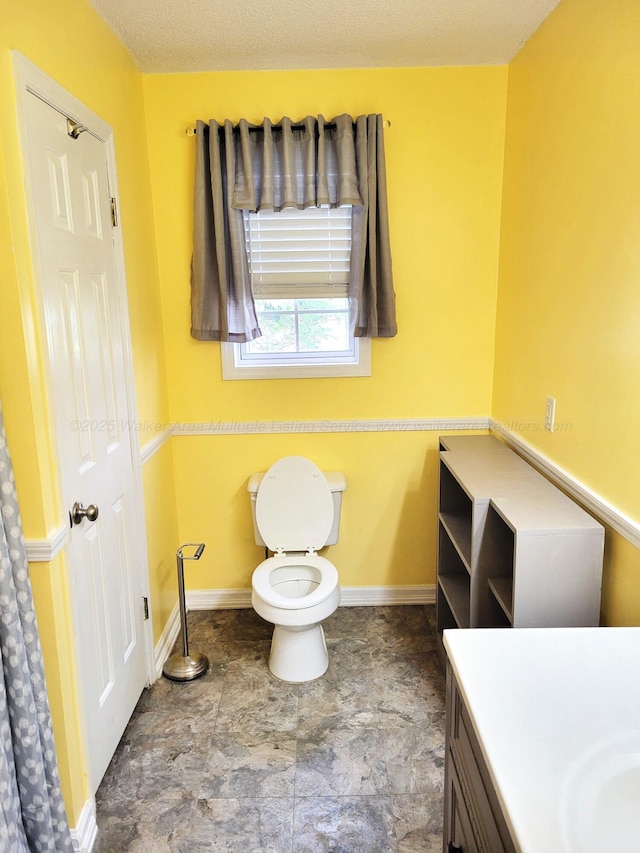 bathroom featuring baseboards, a textured ceiling, toilet, and vanity