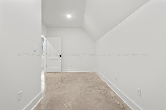 interior space featuring concrete flooring, baseboards, and vaulted ceiling