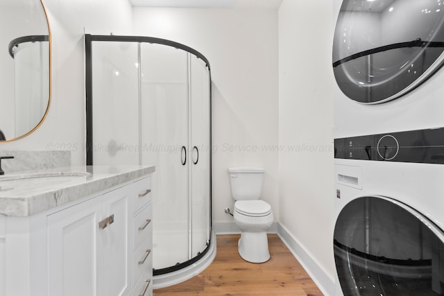 bathroom featuring vanity, toilet, a shower stall, stacked washer / dryer, and wood finished floors