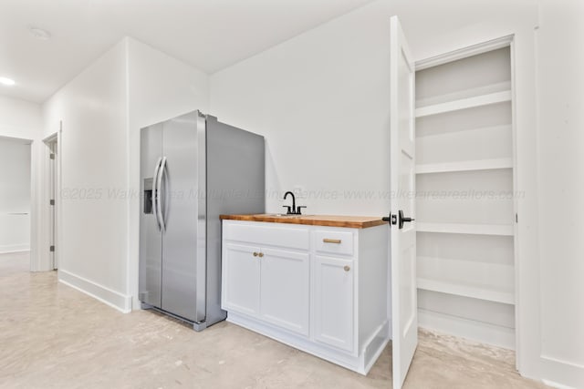 kitchen with white cabinets, wooden counters, concrete floors, a sink, and stainless steel fridge with ice dispenser