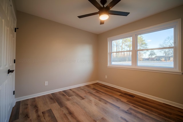 unfurnished room featuring baseboards, visible vents, wood finished floors, and a ceiling fan