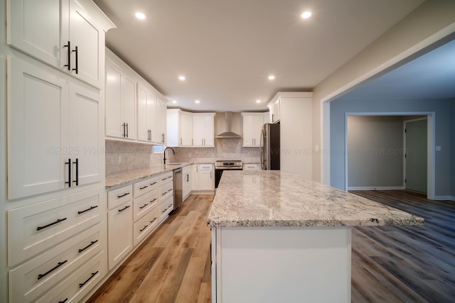 kitchen featuring decorative backsplash, light stone countertops, stainless steel appliances, wall chimney exhaust hood, and a sink
