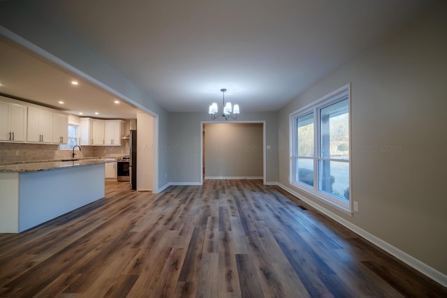 unfurnished living room featuring baseboards, a notable chandelier, a sink, and a healthy amount of sunlight