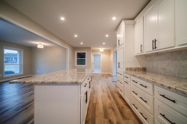 kitchen with backsplash, a kitchen island, light stone counters, white cabinets, and light wood-style flooring