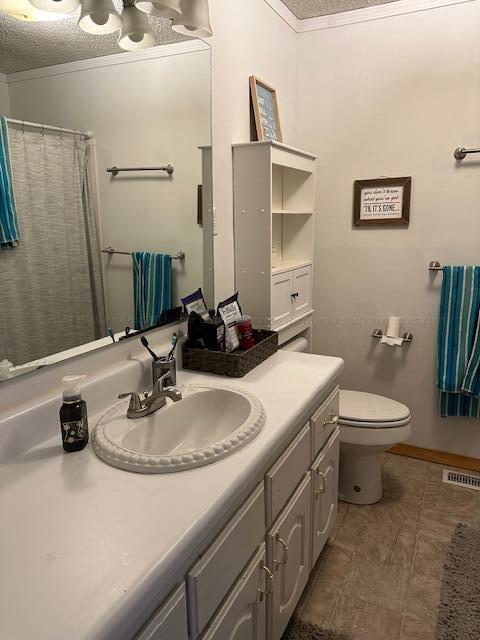 full bath featuring toilet, vanity, a shower with curtain, a textured ceiling, and visible vents