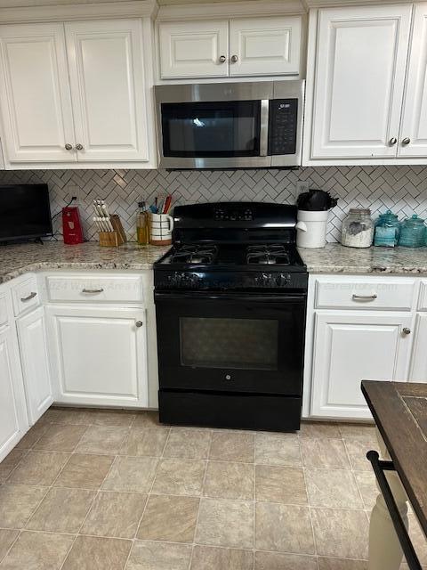 kitchen featuring black range with gas stovetop, light stone counters, white cabinetry, tasteful backsplash, and stainless steel microwave