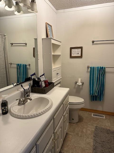 bathroom featuring vanity, toilet, ornamental molding, a textured ceiling, and visible vents