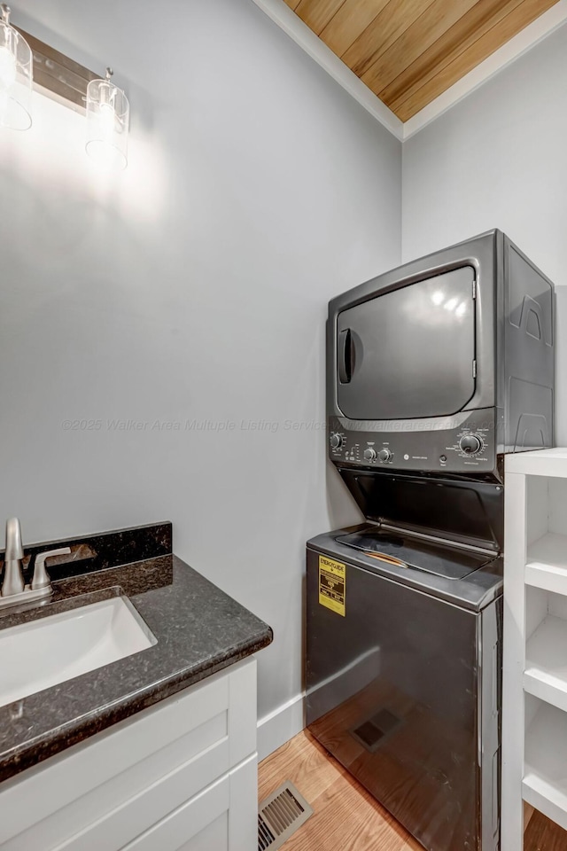 556 Sipsey Rock Rd, Crane Hill, AL 35053 - laundry room featuring baseboards, ornamental molding, a sink, light wood-style floors, and stacked washing maching and dryer