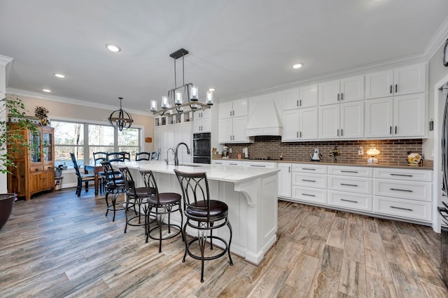 kitchen featuring a breakfast bar, light wood-style floors, a chandelier, premium range hood, and ornamental molding