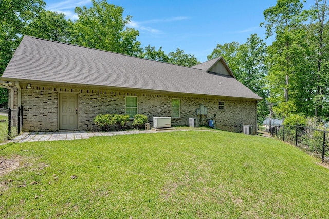 back of house featuring a lawn, brick siding, fence, and a shingled roof