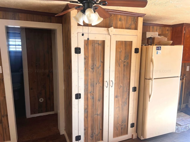 kitchen with ceiling fan, a textured ceiling, white fridge, and wood walls