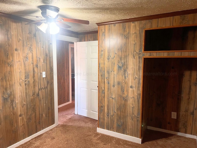 unfurnished bedroom with ceiling fan, wooden walls, a textured ceiling, and dark colored carpet