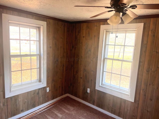 spare room featuring ceiling fan, carpet, a textured ceiling, and wooden walls