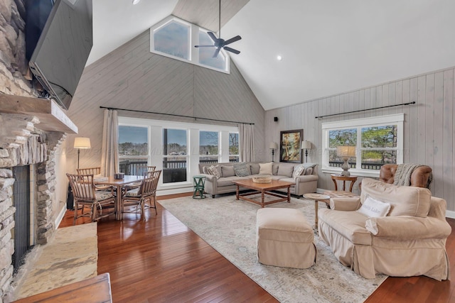 living area featuring a stone fireplace, a wealth of natural light, dark wood-type flooring, and a ceiling fan