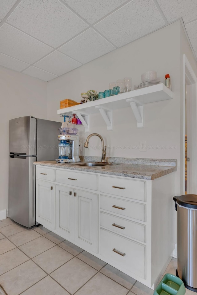 kitchen featuring white cabinets, a sink, a drop ceiling, open shelves, and light tile patterned floors