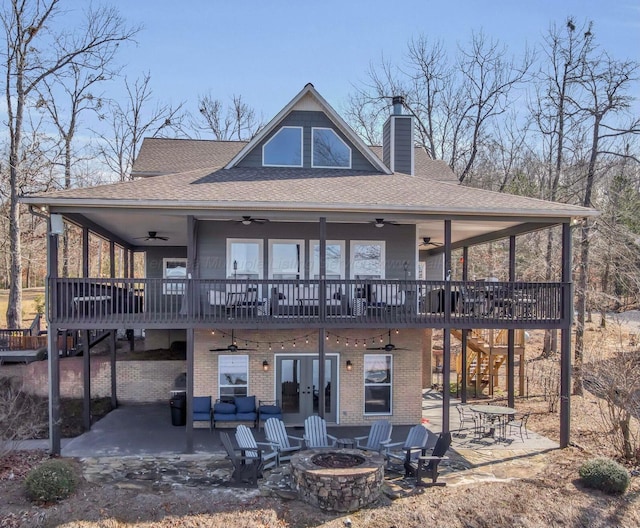back of house featuring roof with shingles, a wooden deck, a patio, an outdoor fire pit, and a chimney