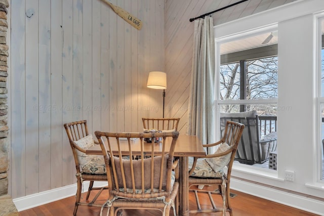 dining area with baseboards, wooden walls, and wood finished floors