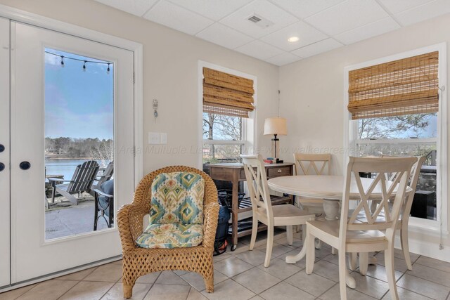 dining space featuring light tile patterned flooring, a water view, visible vents, and a paneled ceiling