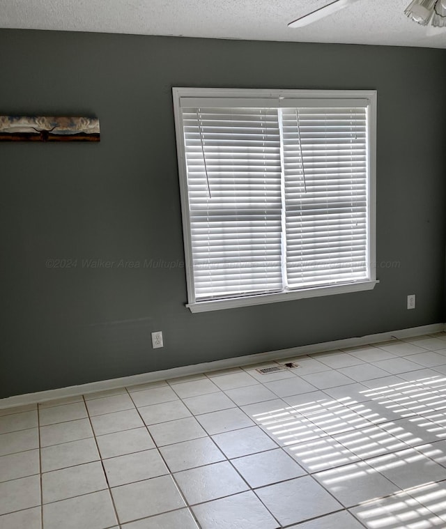 unfurnished room featuring a textured ceiling, light tile patterned floors, plenty of natural light, and baseboards