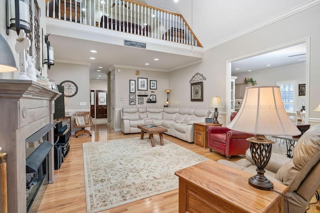 living room with recessed lighting, a fireplace, a towering ceiling, light wood-style floors, and crown molding