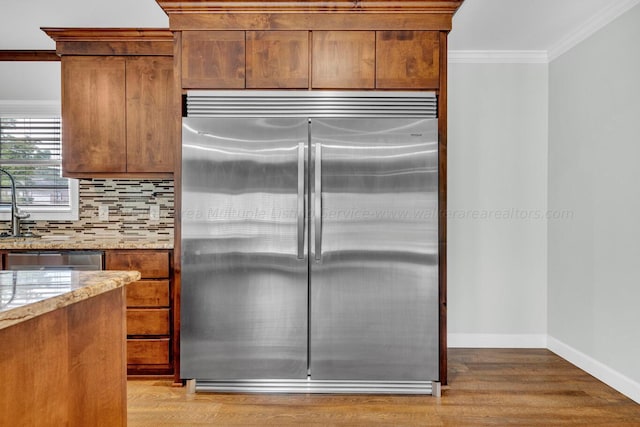 kitchen with light hardwood / wood-style flooring, ornamental molding, appliances with stainless steel finishes, tasteful backsplash, and light stone counters