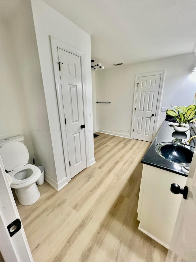 bathroom with visible vents, toilet, a sink, wood finished floors, and baseboards