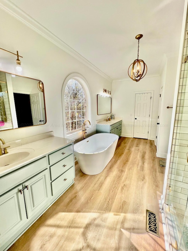 full bathroom featuring a freestanding tub, wood finished floors, two vanities, a sink, and crown molding