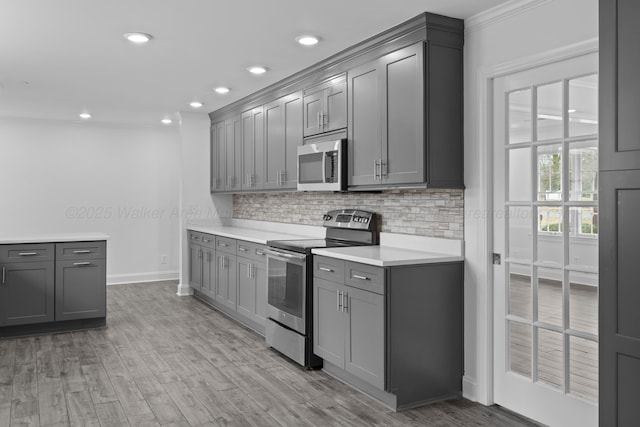 kitchen with light countertops, tasteful backsplash, appliances with stainless steel finishes, gray cabinetry, and light wood-type flooring