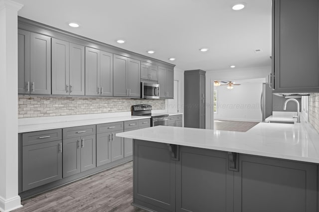 kitchen featuring gray cabinetry, a sink, ceiling fan, a peninsula, and appliances with stainless steel finishes