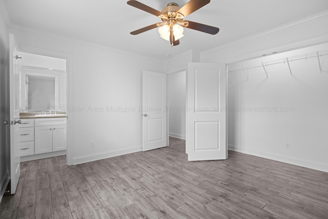 unfurnished bedroom featuring a closet, crown molding, a sink, wood finished floors, and baseboards