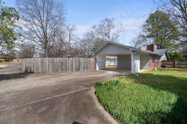 view of side of property featuring concrete driveway, a chimney, fence, a carport, and a yard