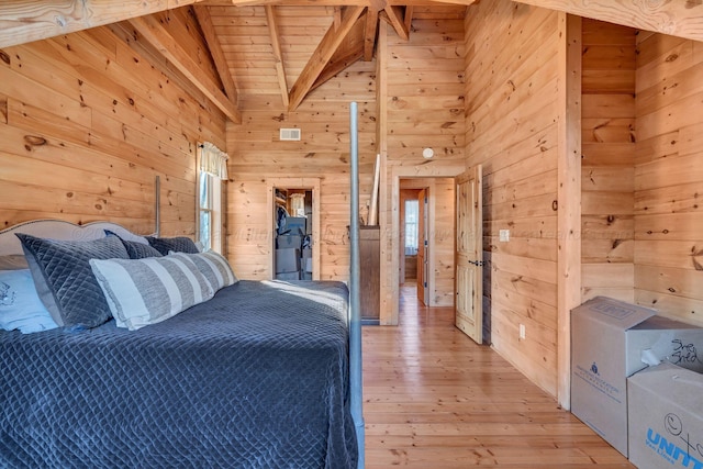 bedroom featuring vaulted ceiling with beams, wooden walls, wood ceiling, light wood finished floors, and visible vents