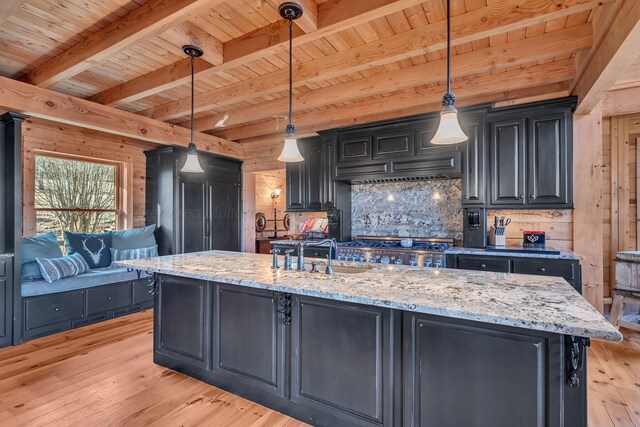 kitchen featuring light wood-style flooring, a sink, dark cabinetry, beamed ceiling, and wood walls
